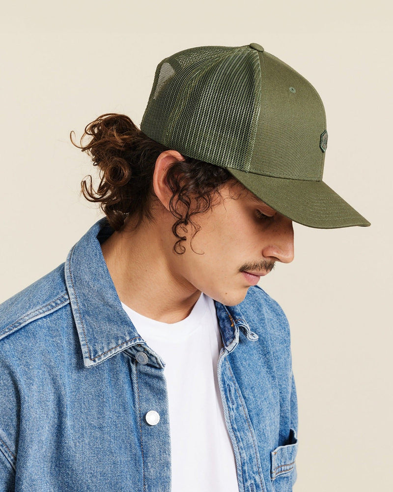 Hemlock male model looking down wearing Cooper Trucker Hat in Olive side profile