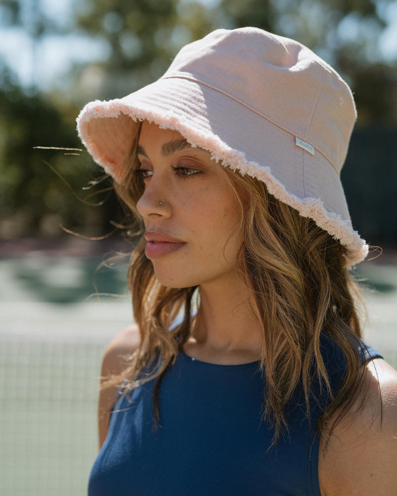 Hemlock female model side profile wearing Coronado Cotton Bucket Hat in Soft Pink sitting down