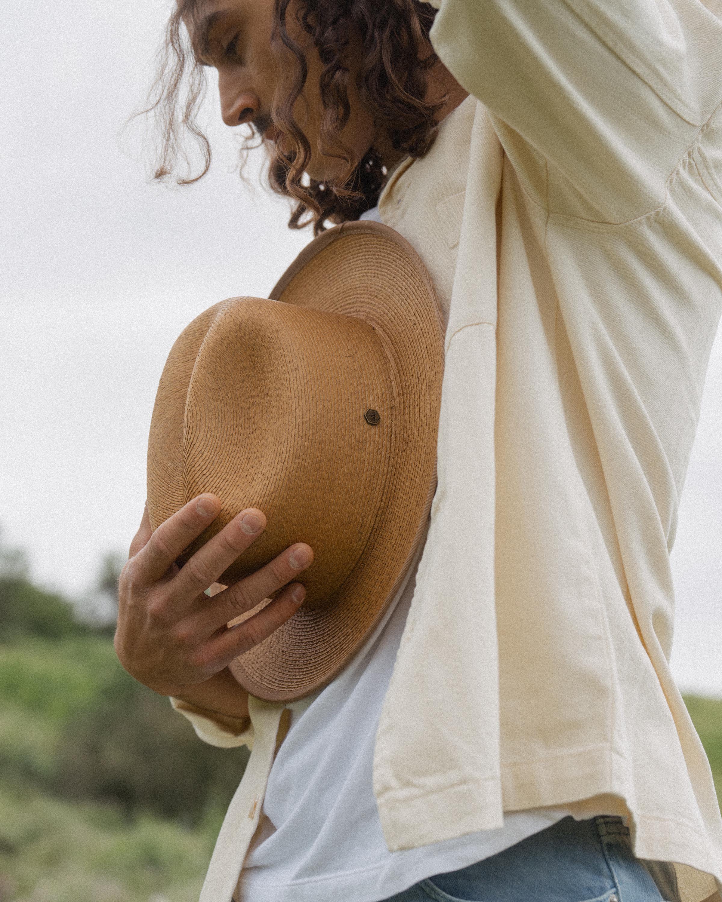 Hemlock male model looking down holding Hemlock Mateo Straw Rancher Hat in Saddle