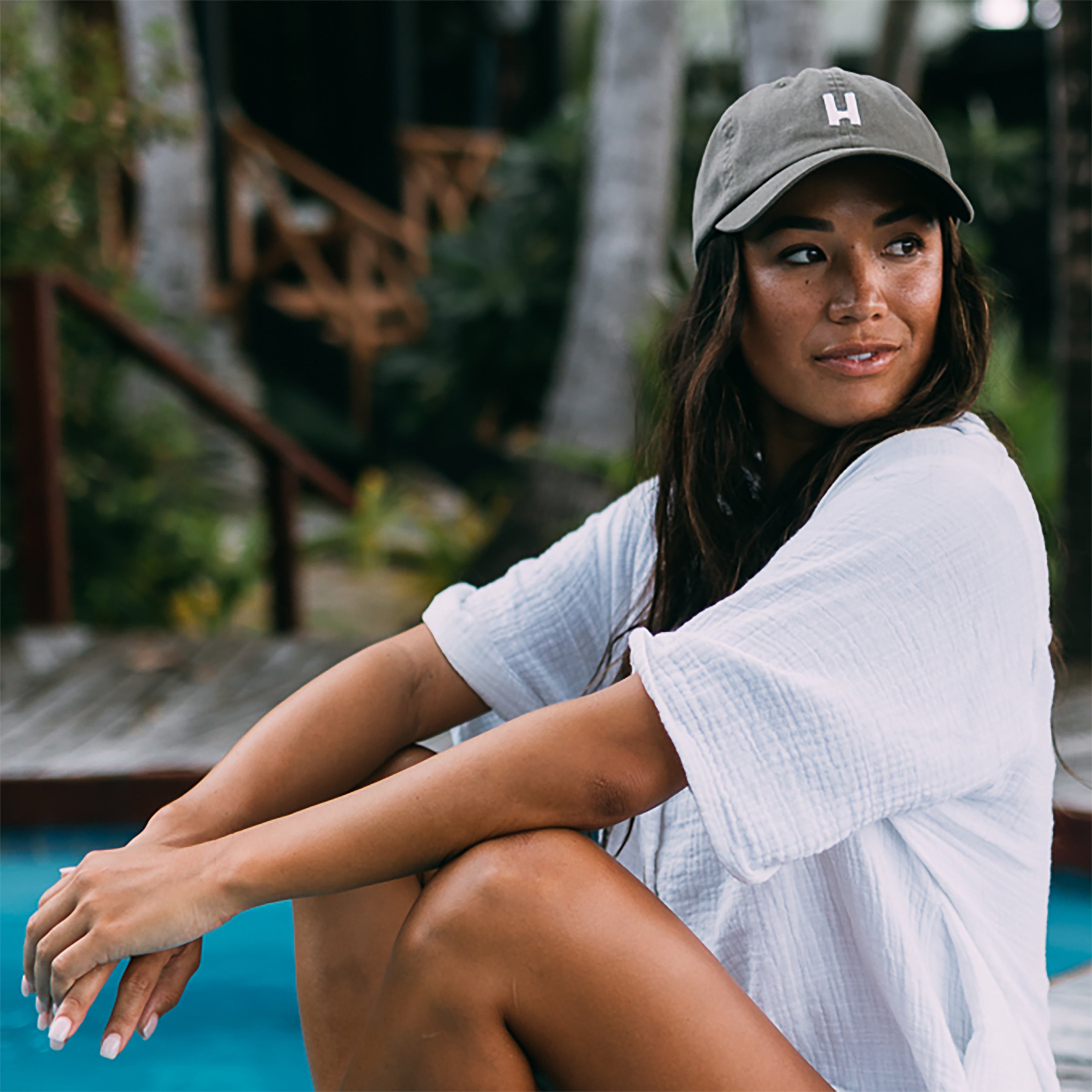 Female model sitting next to pool wearing Hemlock dad hat.