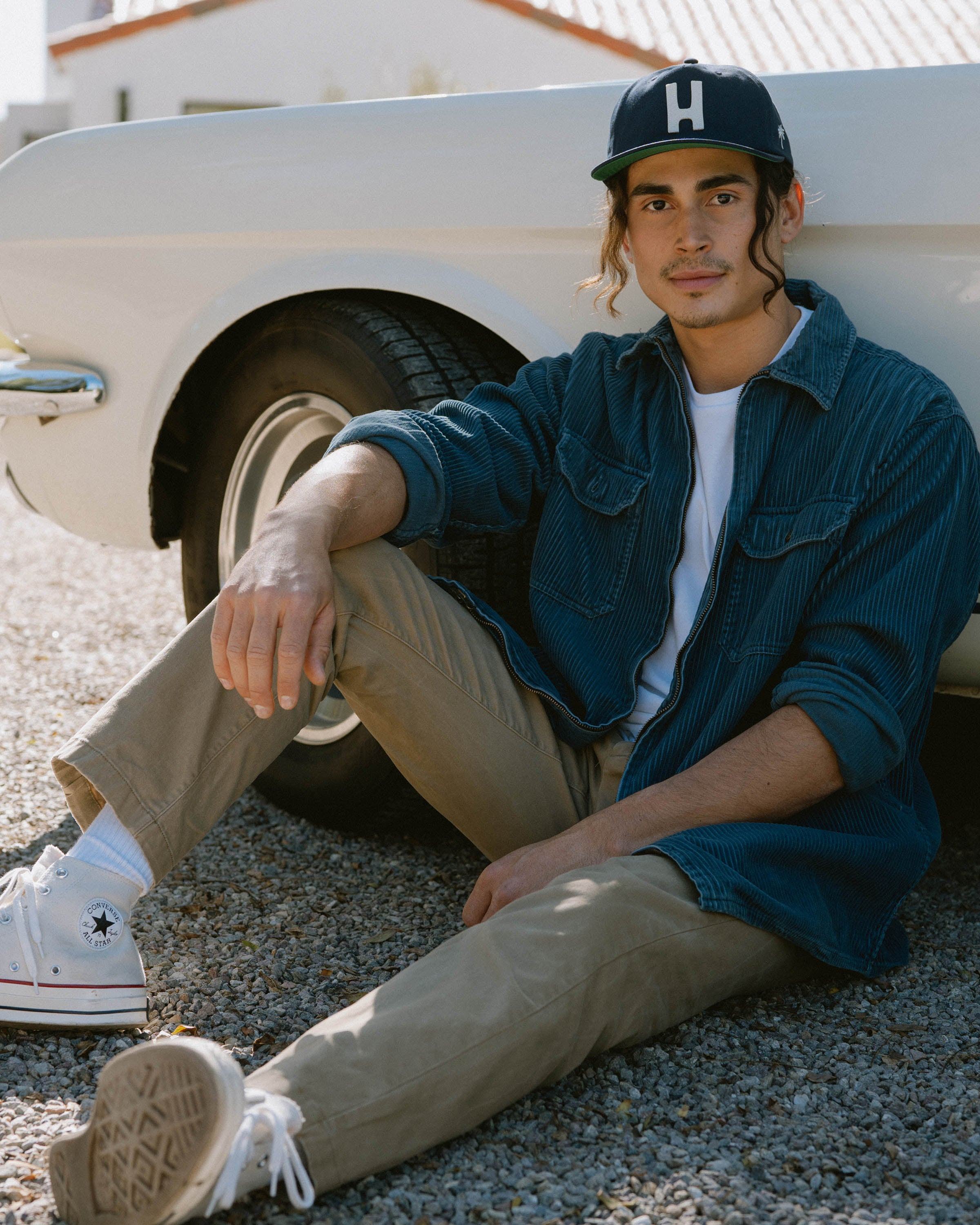 Hemlock male model looking straight wearing Thomas Baseball Hat in Navy sitting down