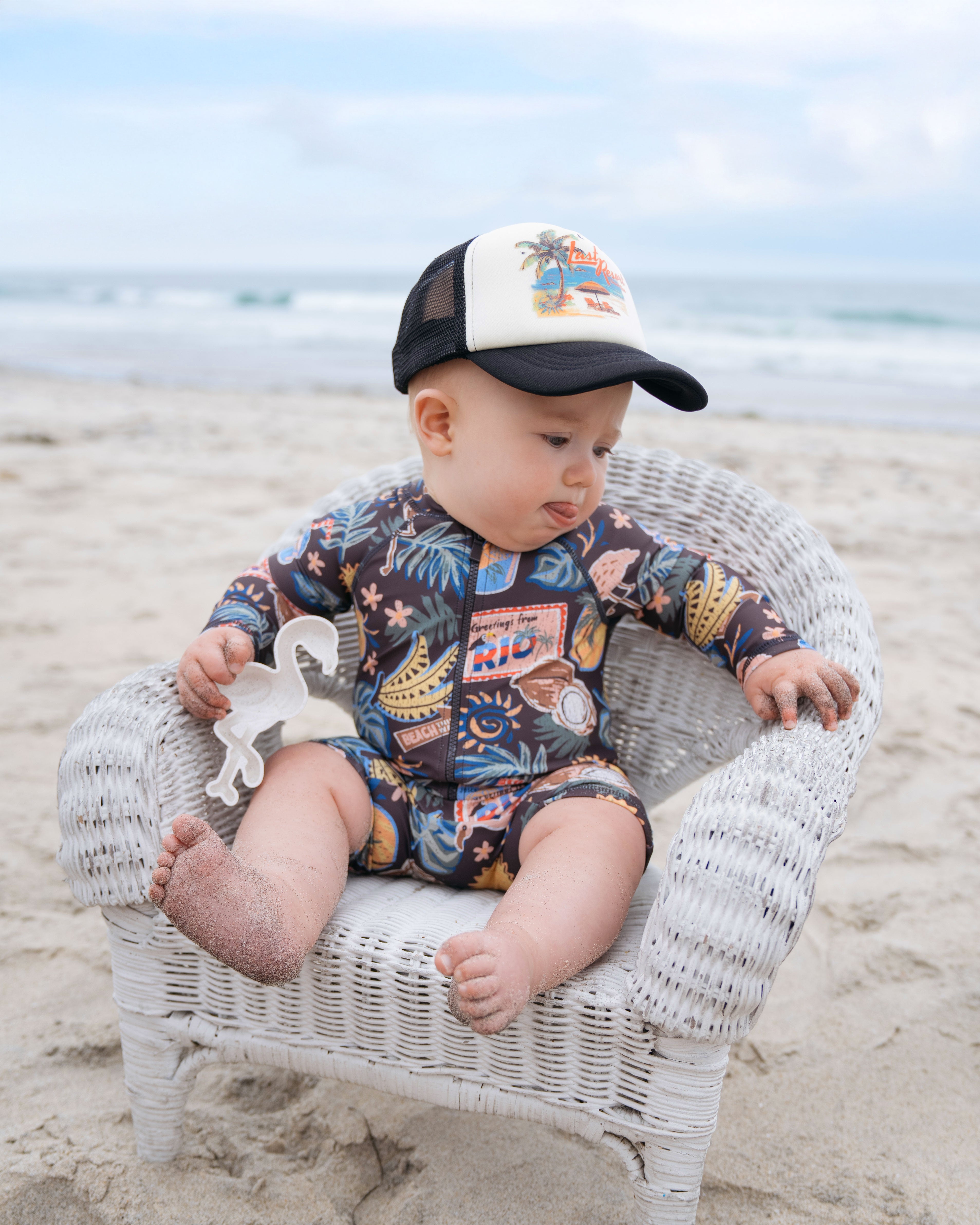 Baby sitting on a small chair at the beach wearing Hemlock Foam Trucker Ball Cap