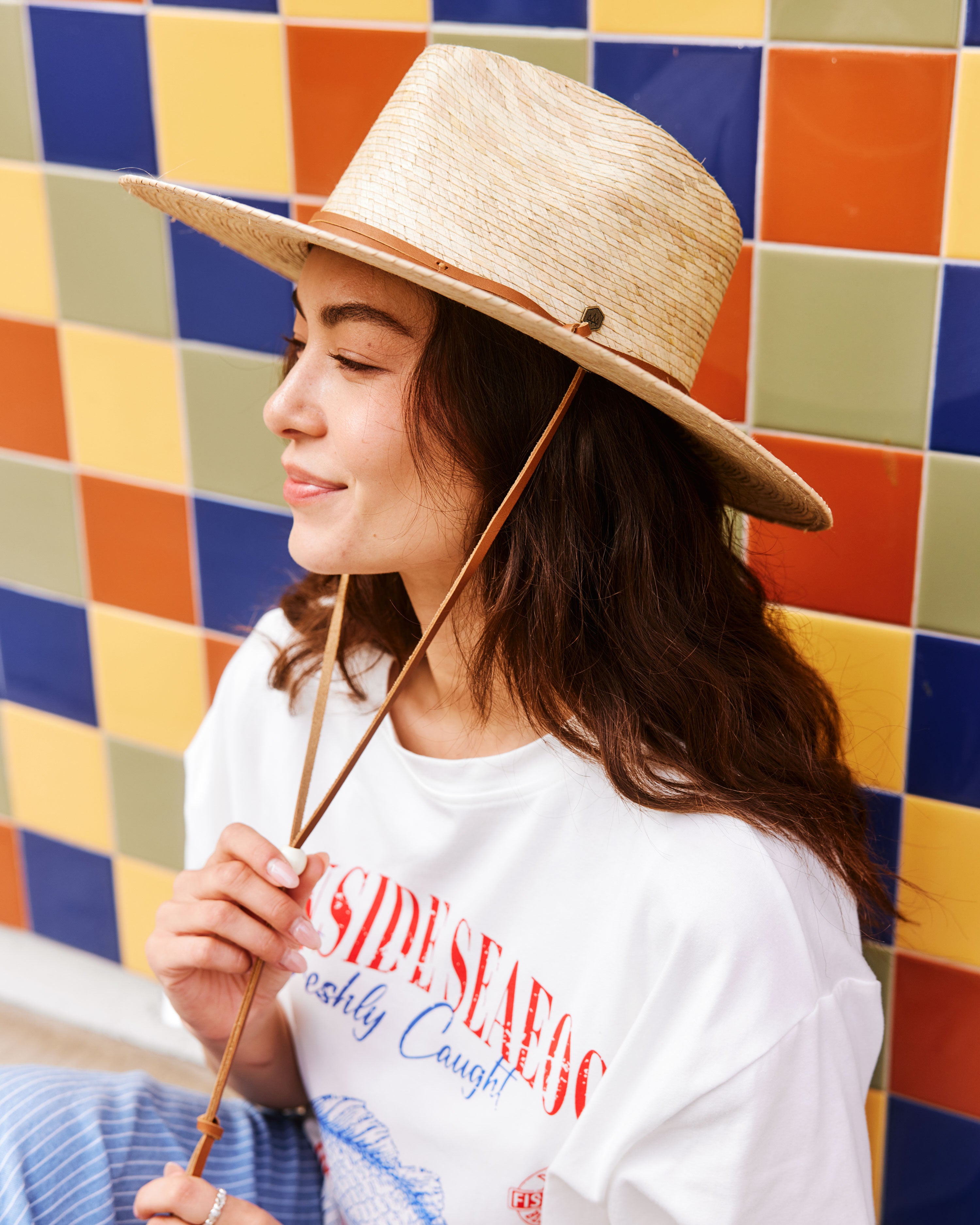 Hemlock female model wearing the Morro Fedora Straw Hat in Natural in front of colorful wall