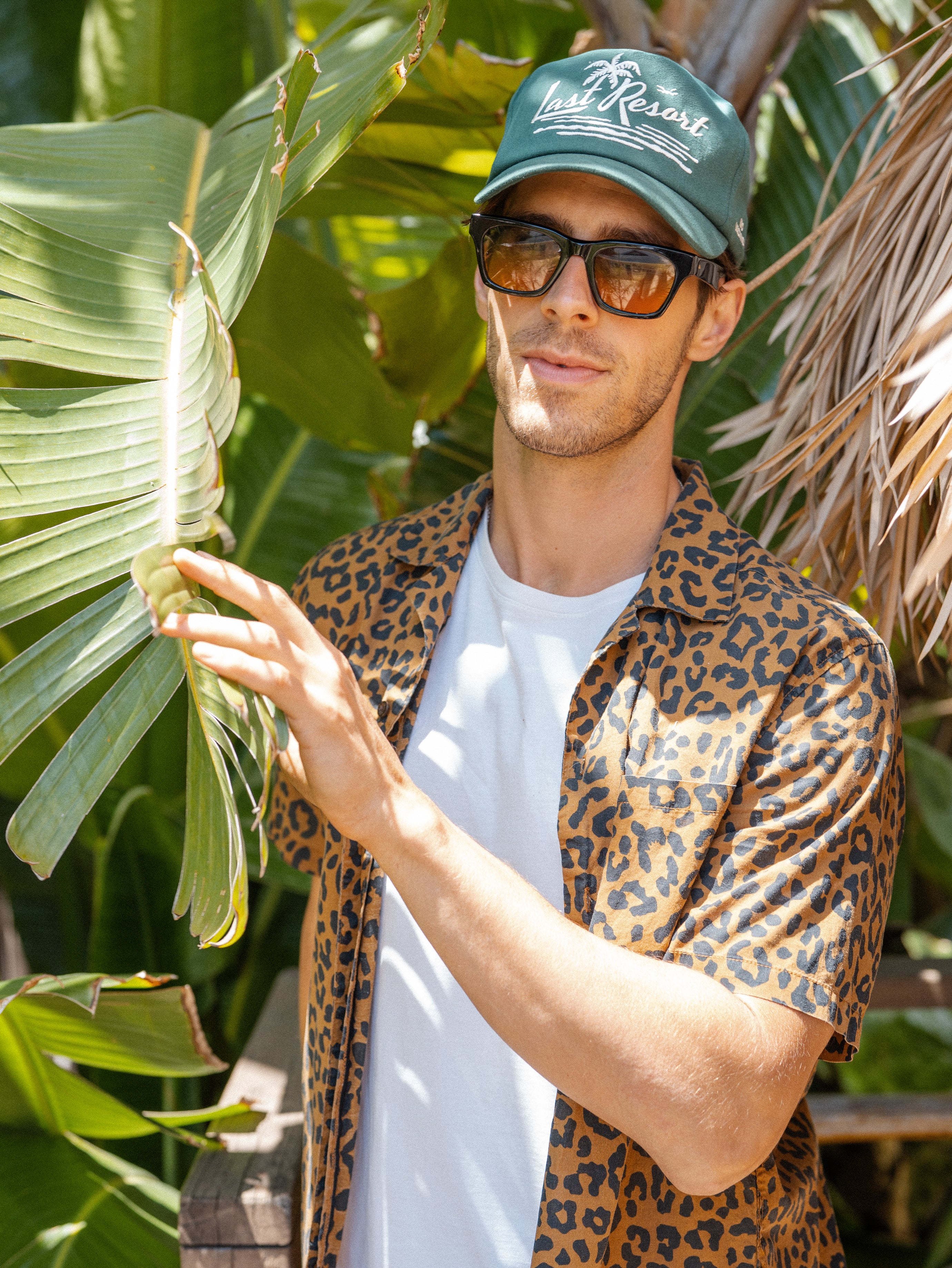 Hemlock male model wearing the Last Resort Baseball Hat in Green by palm tree