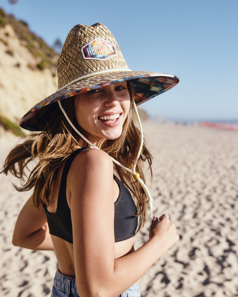 Hemlock female model looking back wearing Bowie straw lifeguard hat with Tie Dye pattern running at the beach