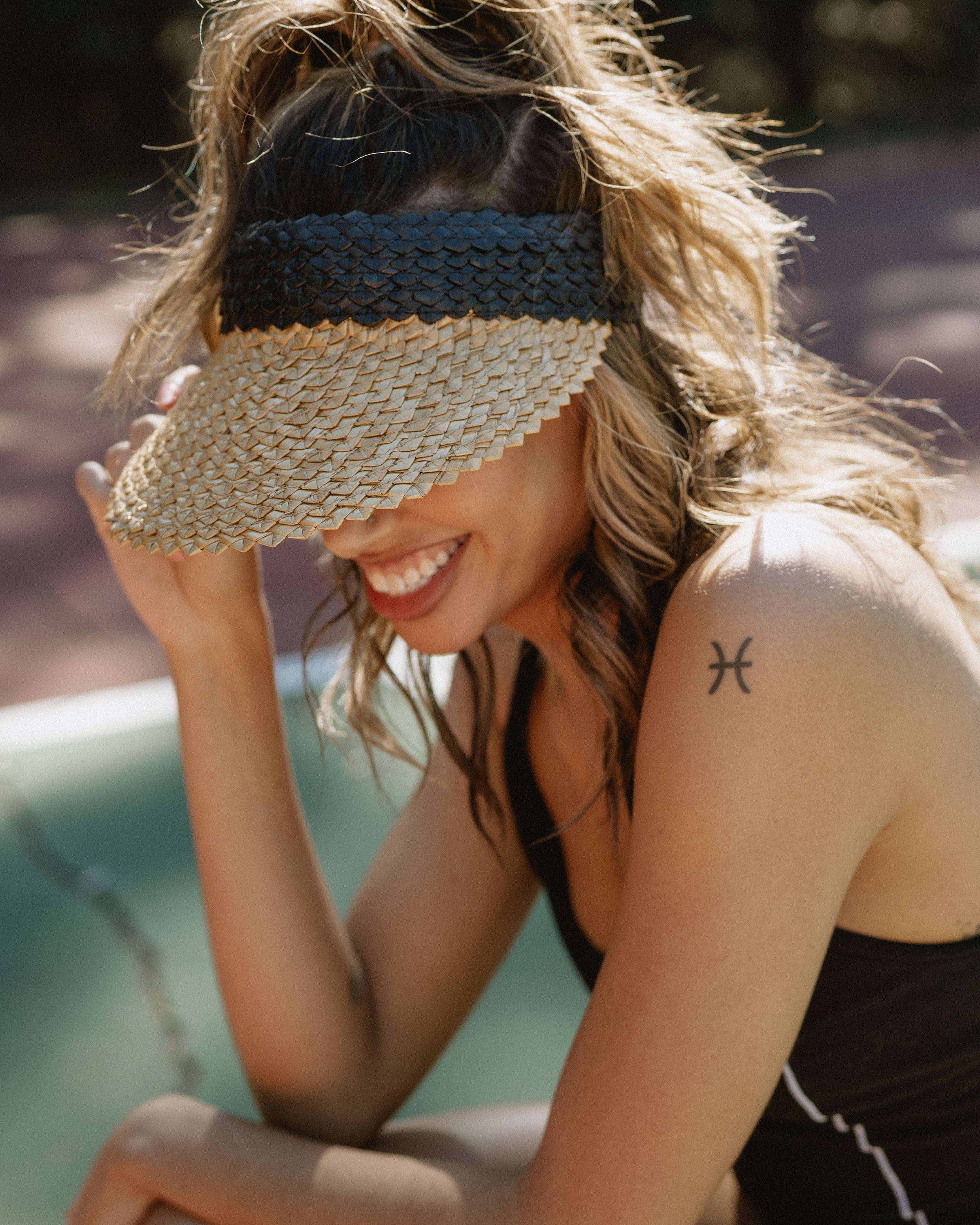 Hemlock female model looking down wearing  Capri Straw visor in Black and Tan