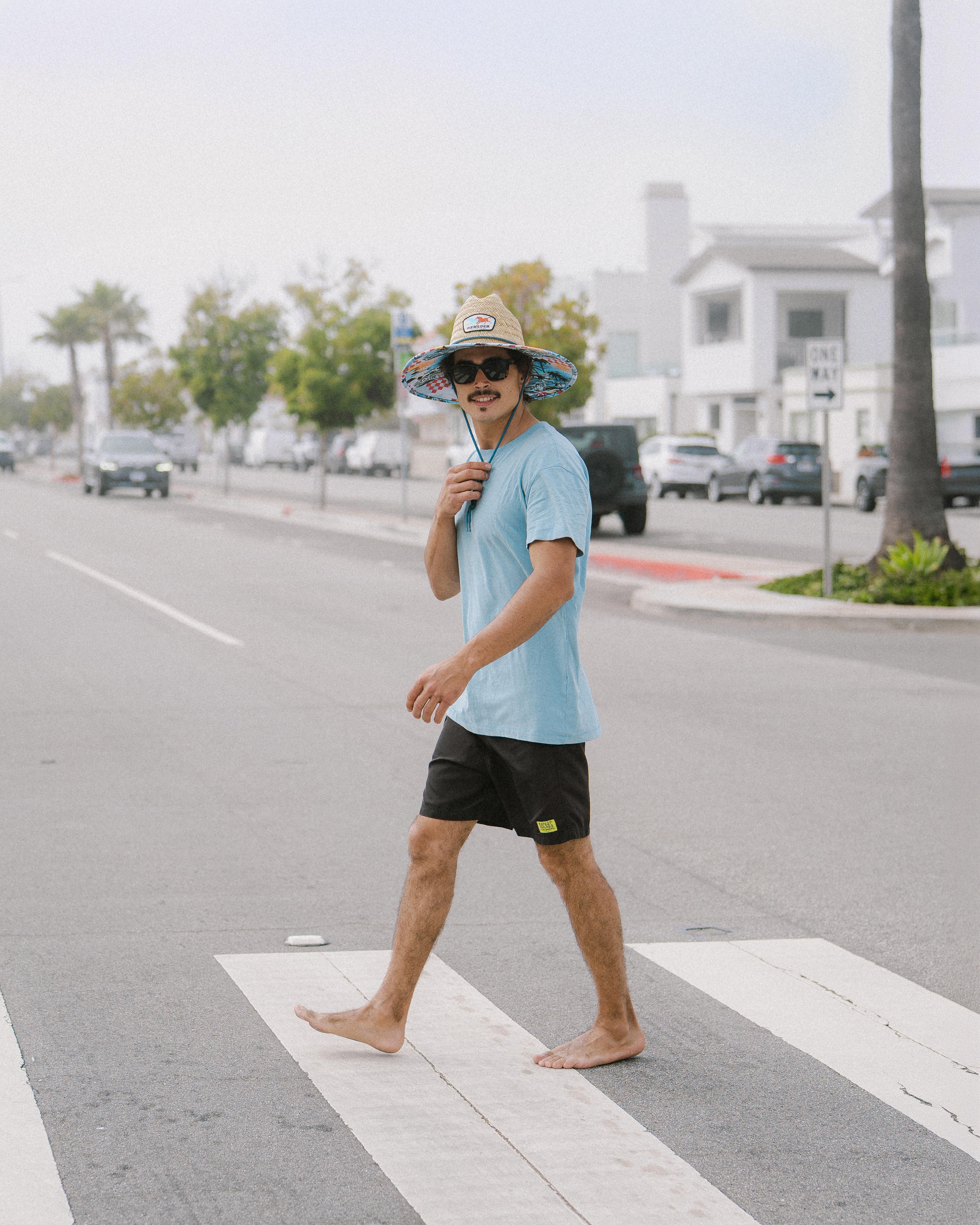 Hemlock male Model wearing the
UPF50+ Lifeguard hat in Racing Legend print crossing the street