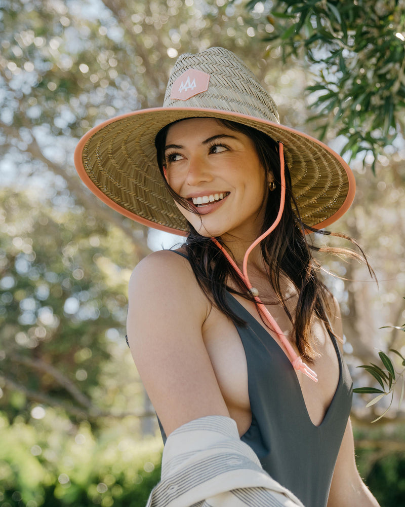 Hemlock female model looking left wearing Guava straw lifeguard hat with coral color