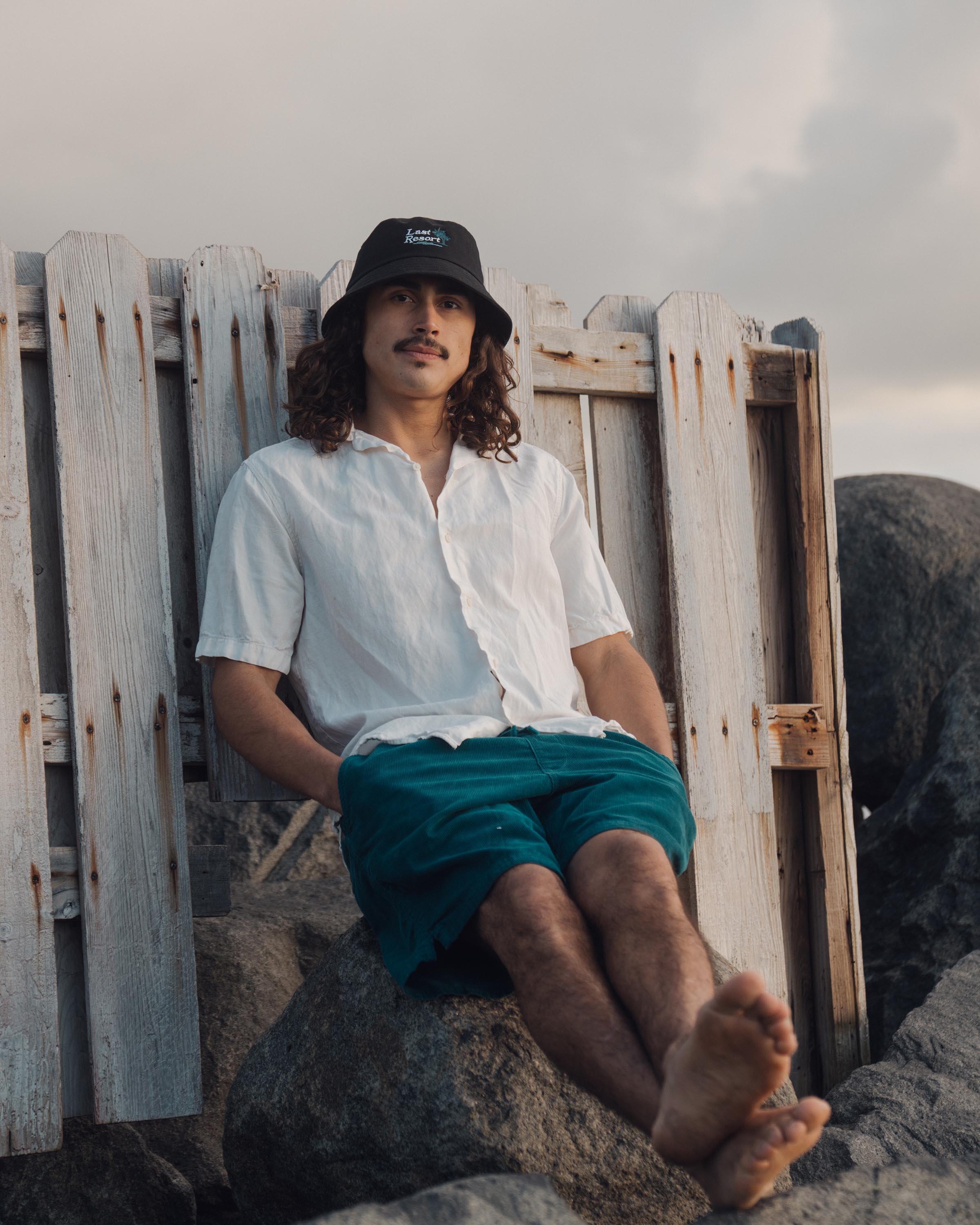 Hemlock male model looking straight wearing Hemlock Last Resort Cotton Bucket Hat in Black sitting down