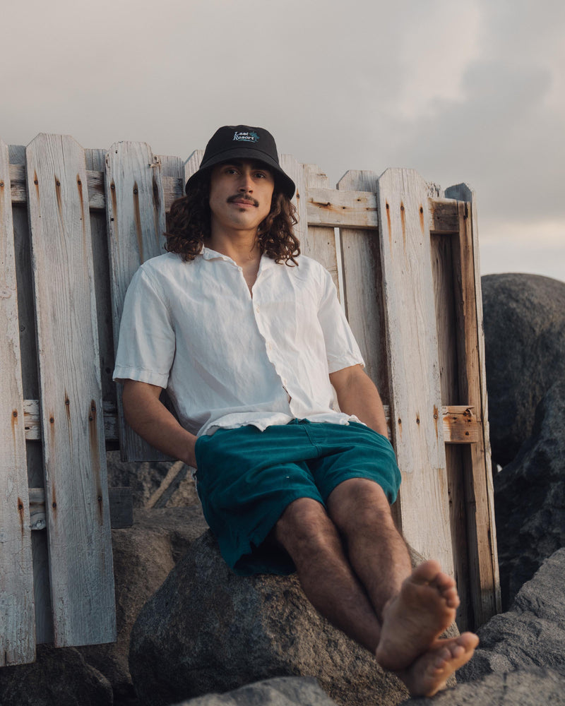 Hemlock male model looking straight wearing Hemlock Last Resort Cotton Bucket Hat in Black sitting down