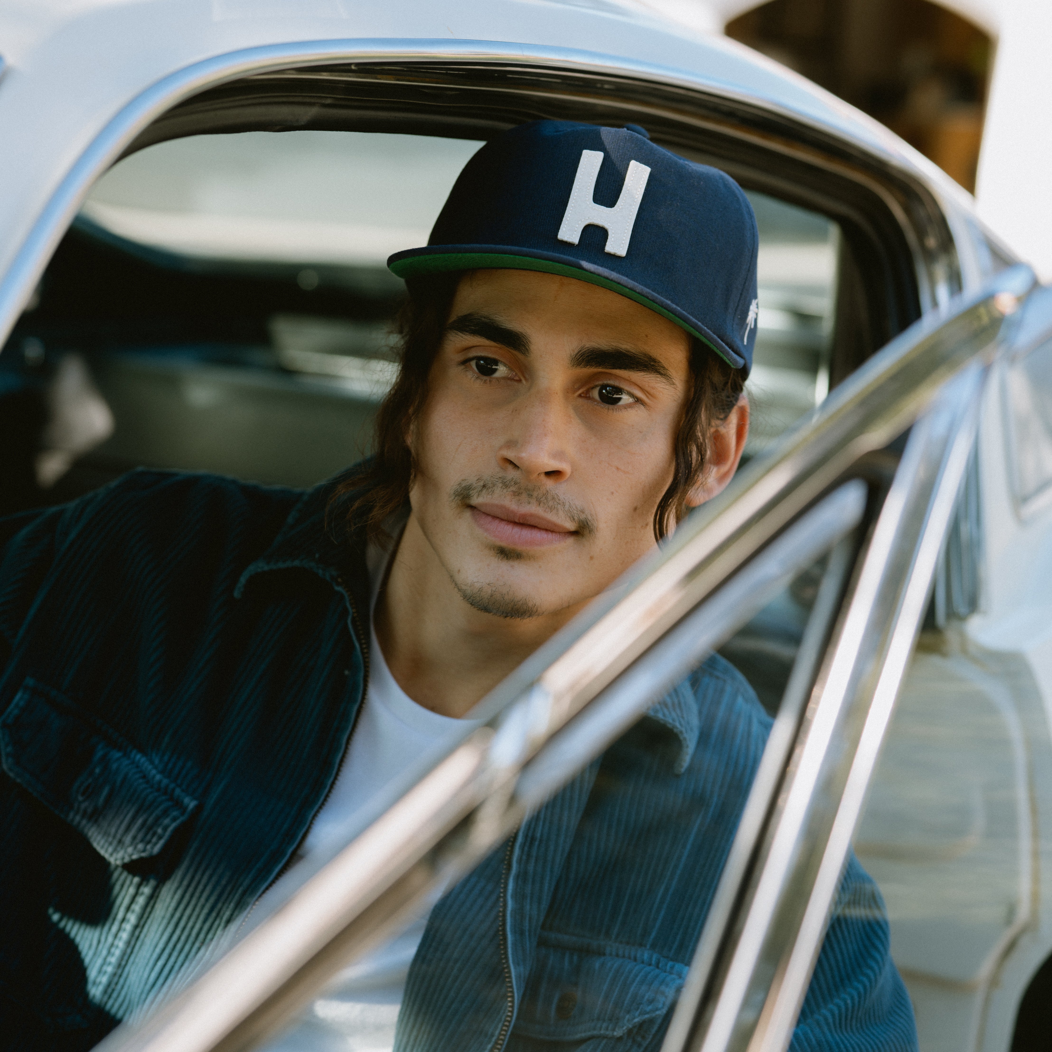 Male model wearing Thomas baseball hat sitting in vintage Mustang.