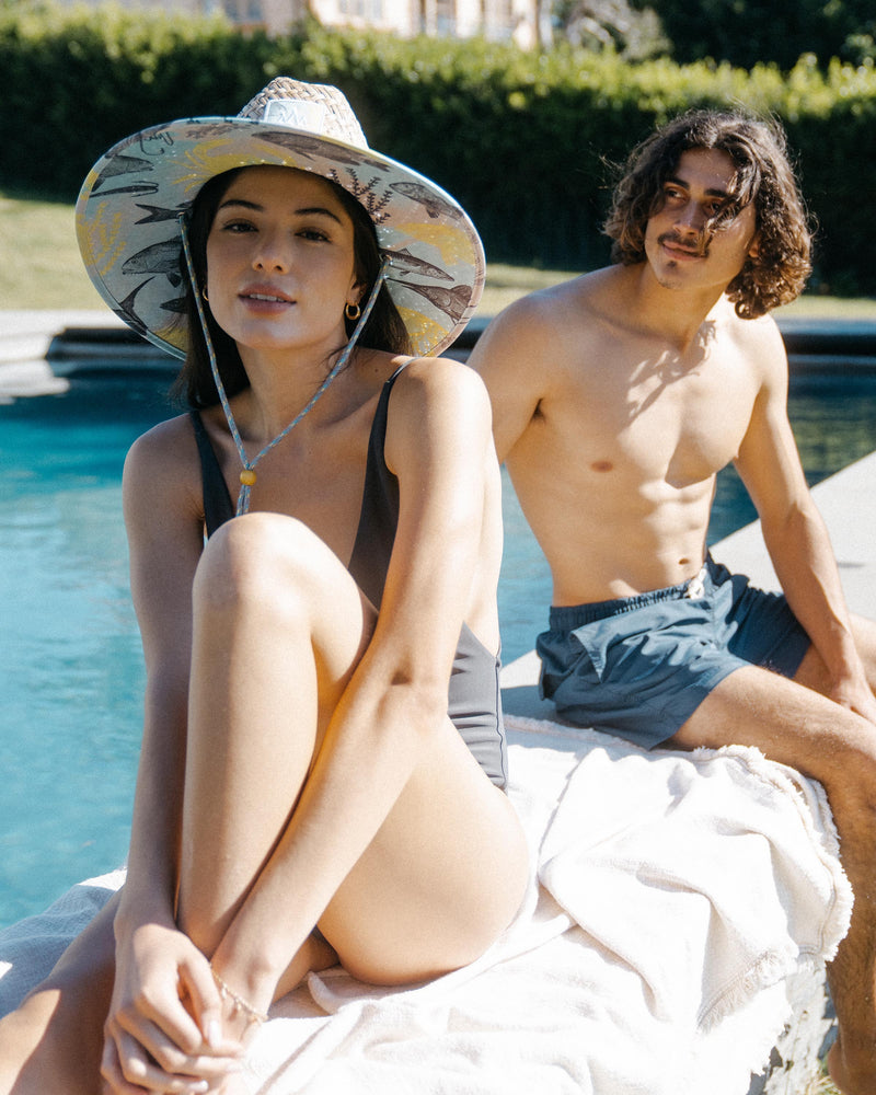 Hemlock female model looking straight wearing Skipper straw lifeguard hat with saltwater neon pattern by the pool