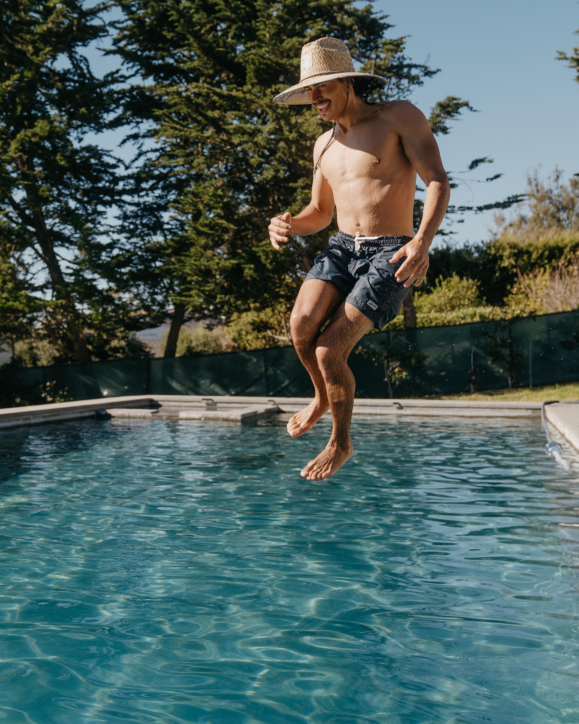 Hemlock male model jumping in the pool wearing Skipper straw lifeguard hat with saltwater neon pattern