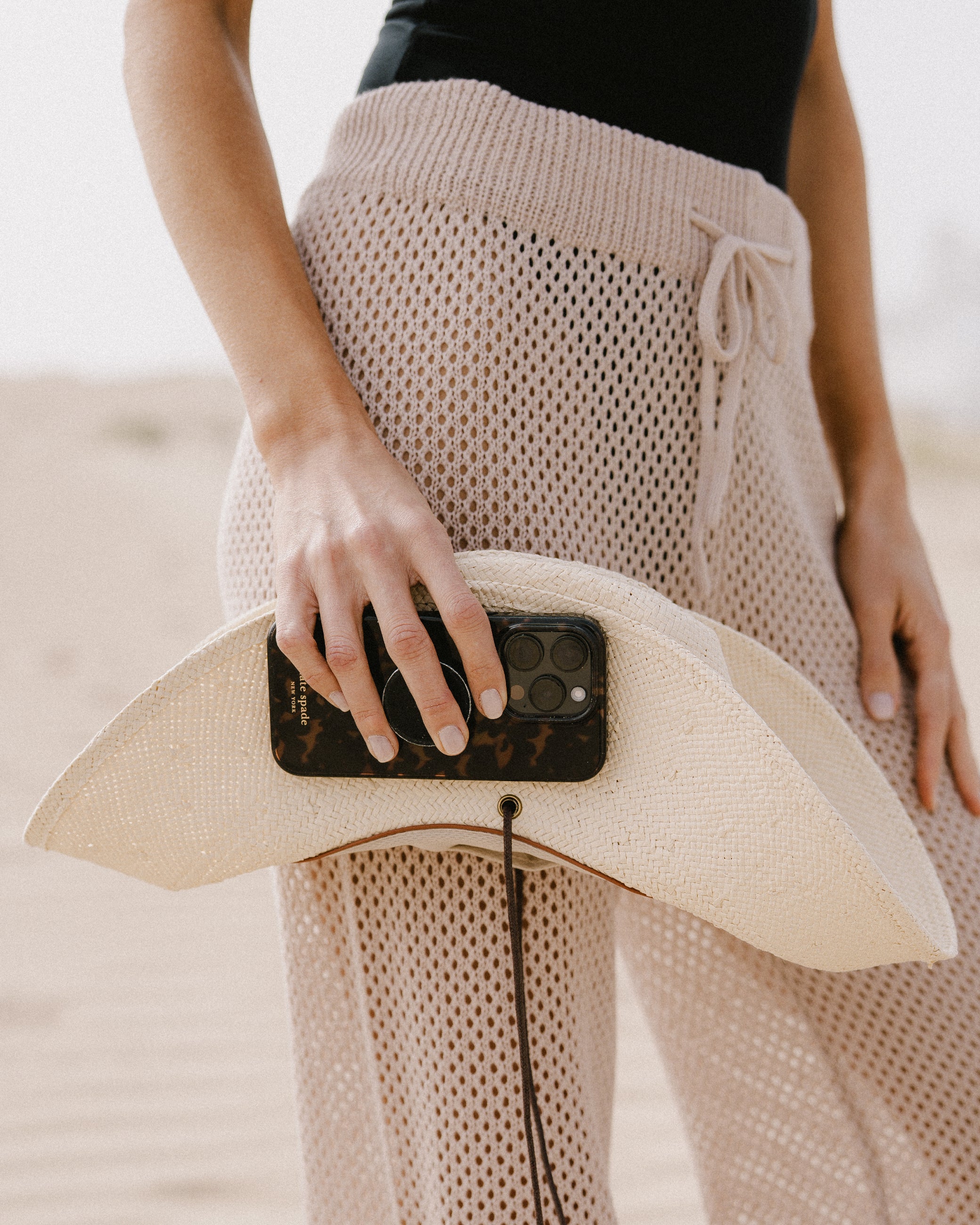 Person holding a smartphone with a straw hat on a blurred beach background