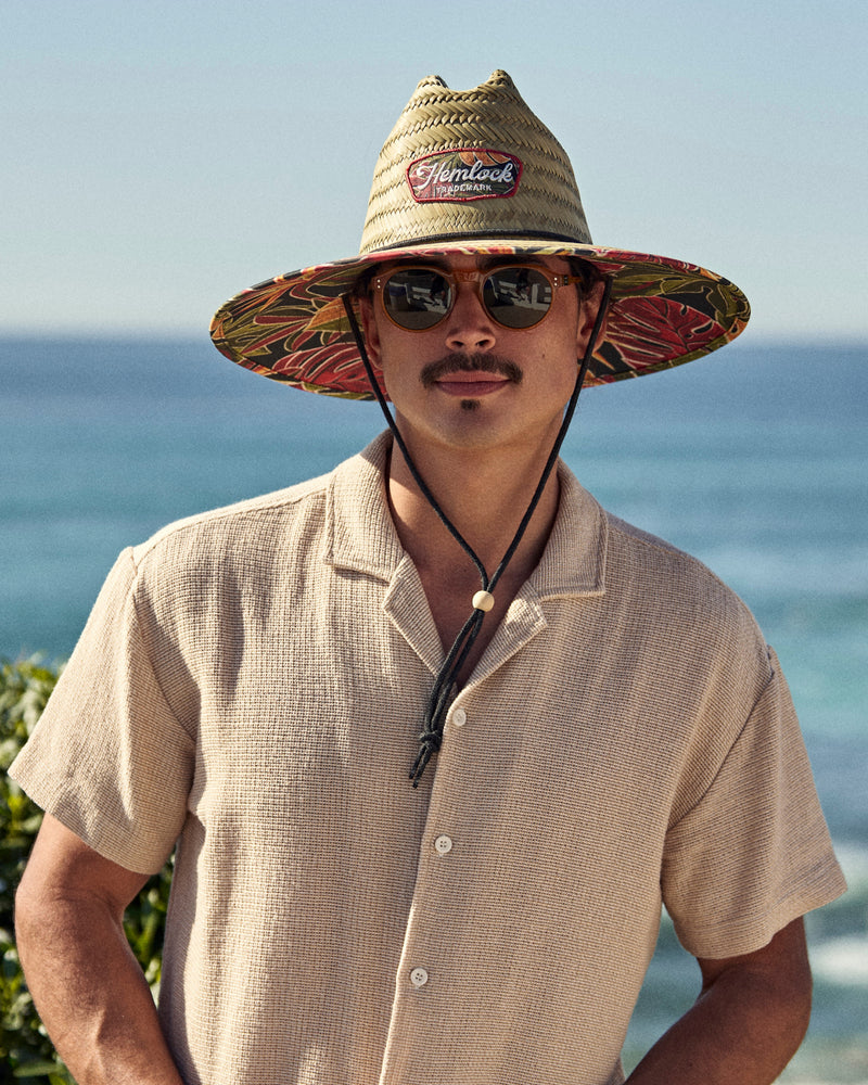 Hemlock male model wearing the UPF50+ Lifeguard hat in tropical foliage print in front of the ocean